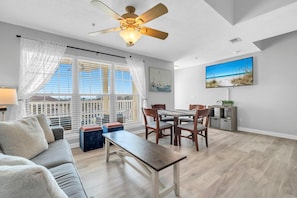 Ein modernes Wohnzimmer mit einer Couch, einem Esstisch, Stühlen, einem Deckenventilator und einem an der Wand befestigten Fernseher.