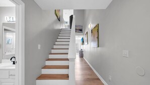 Eine Treppe mit Holzstufen und weißen Wänden, die zu einem Raum mit Waschbecken und einer Tür führt.