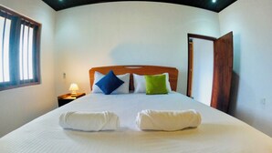 A neatly made bed with pillows and towels, a wooden headboard, a nightstand with a lamp, and a window with blinds. - Cozy 1-bedroom villa in awesome Tangalle with AC (Tangalle)