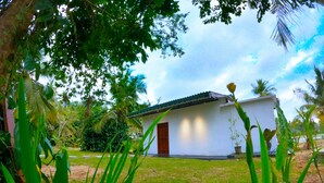A small white building with a dark door, surrounded by lush greenery and palm trees. - Cozy 1-bedroom villa in awesome Tangalle with AC (Tangalle)