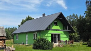 A green house with a sloped roof, a front door, and a small porch with chairs.