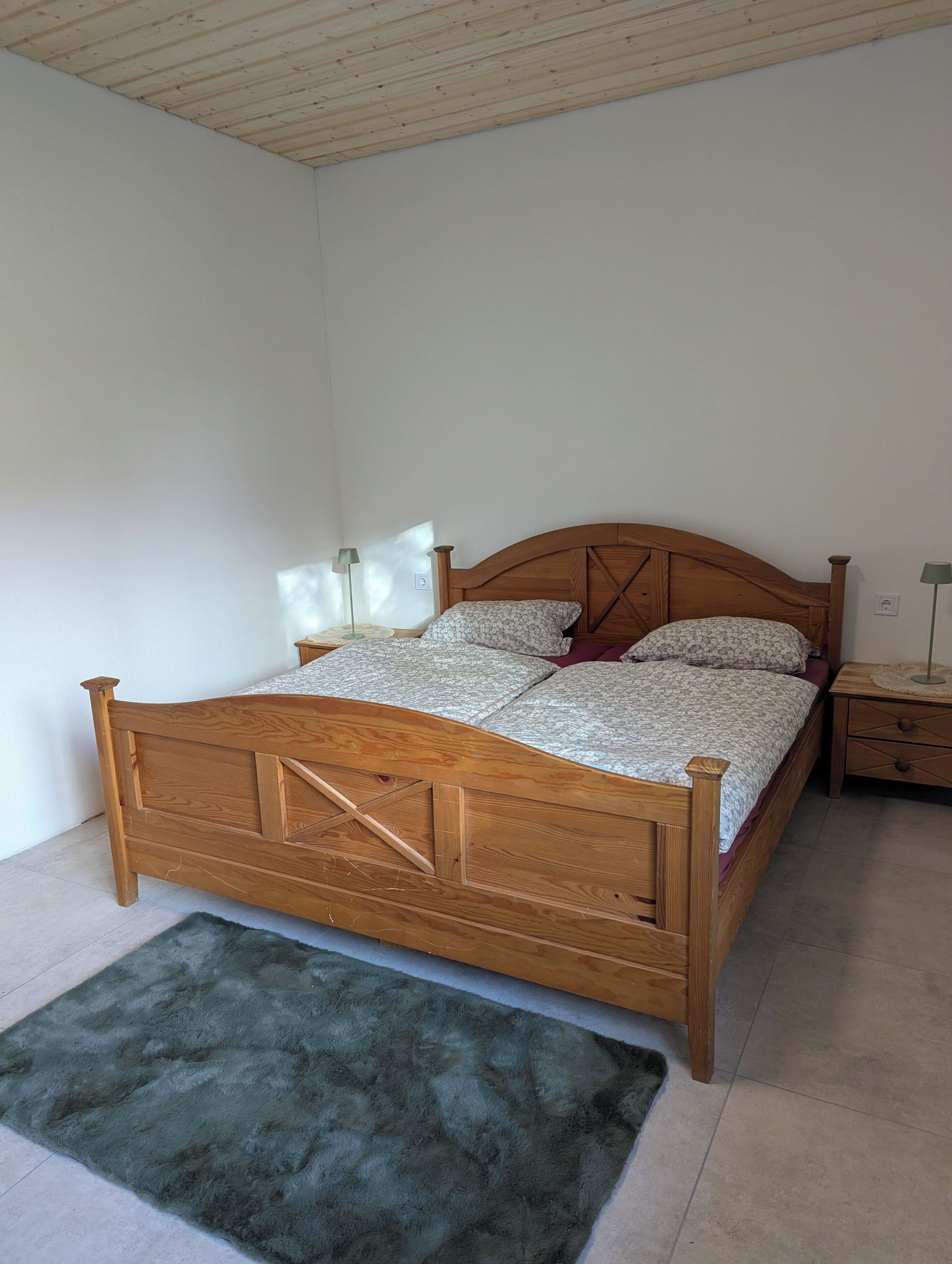 Una cama de madera con cabecera, una mesita de noche y un tapete verde.