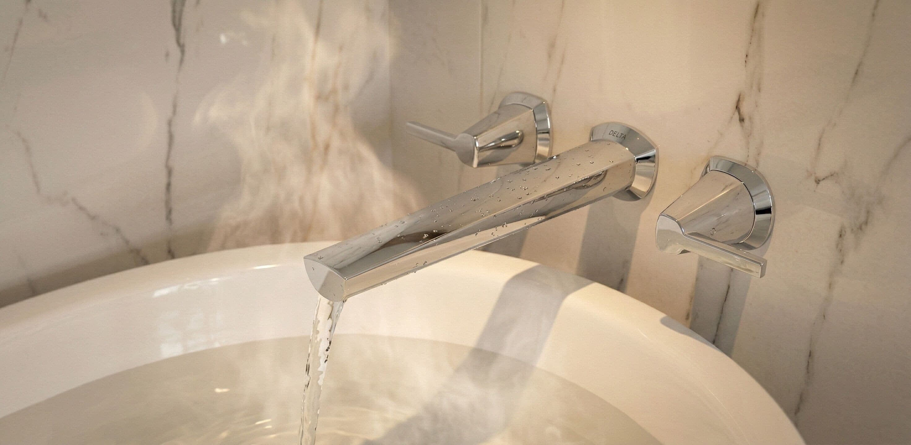 A bathtub with water running, a Delta faucet, and a marble wall in the background.
