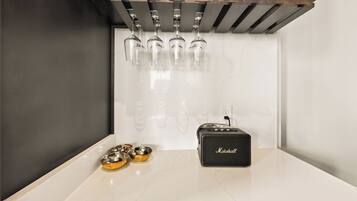 A kitchen with a marble countertop, hanging wine glasses, a black speaker, and two pet bowls.