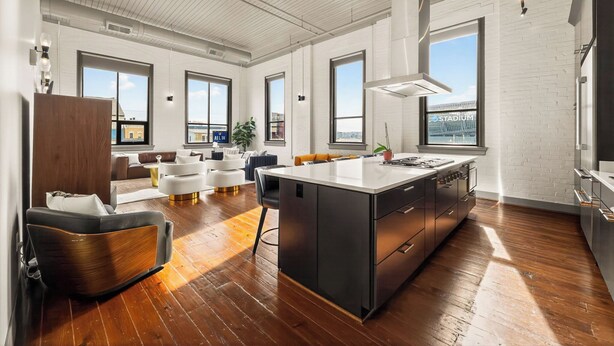 A spacious kitchen with a large island, white brick walls, and large windows.