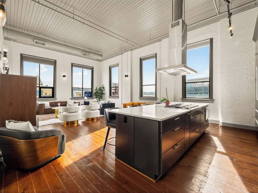 Una cocina amplia con una isla grande, paredes de ladrillo blanco y ventanas grandes.