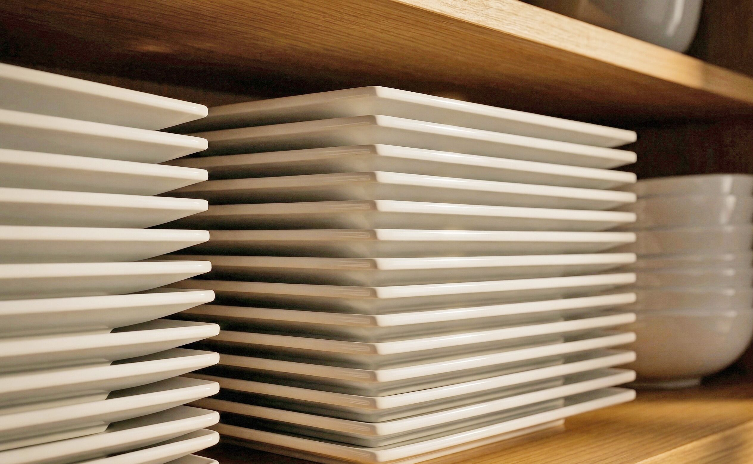 A stack of white plates on a wooden shelf.