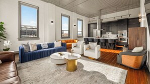 A modern living room with a sofa, chairs, a coffee table, and a kitchen area with appliances.
