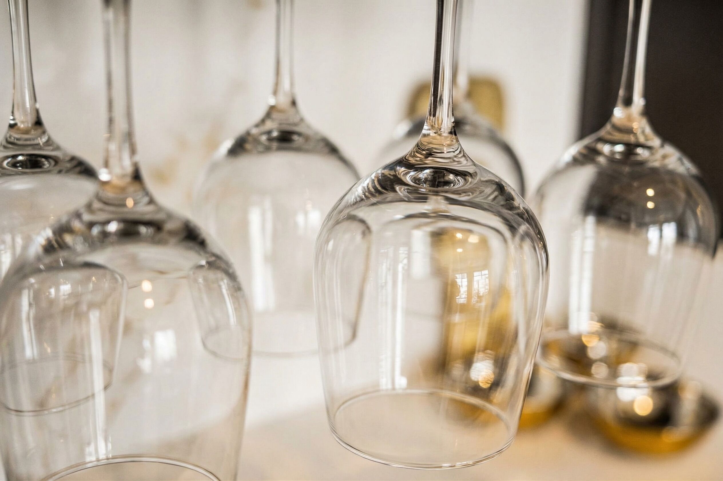 A close-up of several clear wine glasses with a unique design, hanging from a bar area.