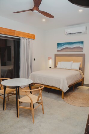 A bedroom with a bed, a ceiling fan, an air conditioning unit, a round table with chairs, and a painting on the wall. - Hotel calma celesti (Elota)