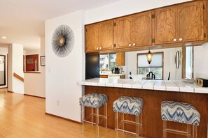 Eine moderne Küche mit Holzschränken, einer weißen Arbeitsplatte und drei Barhocker mit gemusterten Sitzkissen.