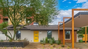 Ein modernes Haus mit gelber Tür, ein Baum im Vorgarten und eine Holzw pergola.