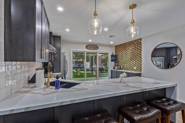 A modern kitchen with a marble countertop, dark cabinetry, and a large island with bar stools. - Modern  dwn twn 3BR/3BR W/ pool & spa (Phoenix)