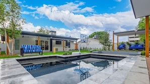 Ein modernes Haus mit Swimmingpool, Basketballkorb und überdachter Sitzgelegenheit.