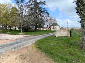A rural road leading to a white building with a red roof, surrounded by trees and a large rock with 'COLONGES' inscribed.
