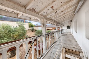 Un espace extérieur abrité, doté d’une terrasse en bois, de rampes blanches et offrant une vue sur les bâtiments et la végétation environnants.