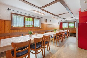 Un espace repas avec des lambris en bois, des tables recouvertes de nappes blanches et des chaises dotées de coussins.