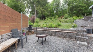 An outdoor patio with a wooden bench, a metal grill, and a stone wall.