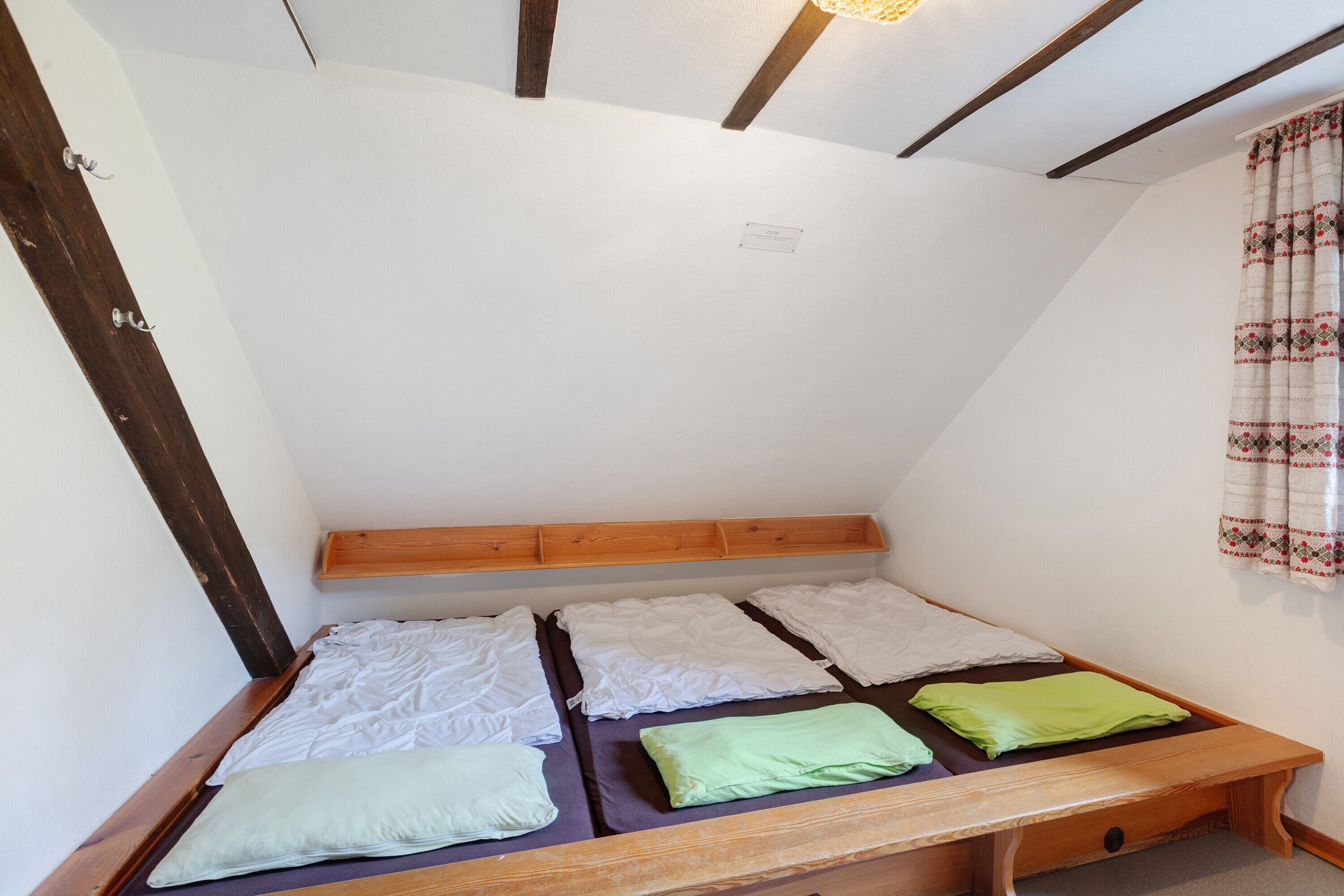 A small, single-bed room with a wooden headboard and a bench at the foot of the bed.