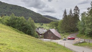 A rural landscape with a wooden house, a red car, and a motorcycle on a road.
