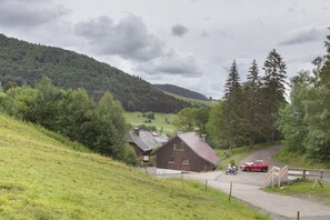 Un paysage rural avec une maison en bois, une voiture rouge et une moto sur une route.