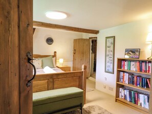 A bedroom with a wooden bed, a bedside table with a lamp, a bookshelf, and a clock on the wall.