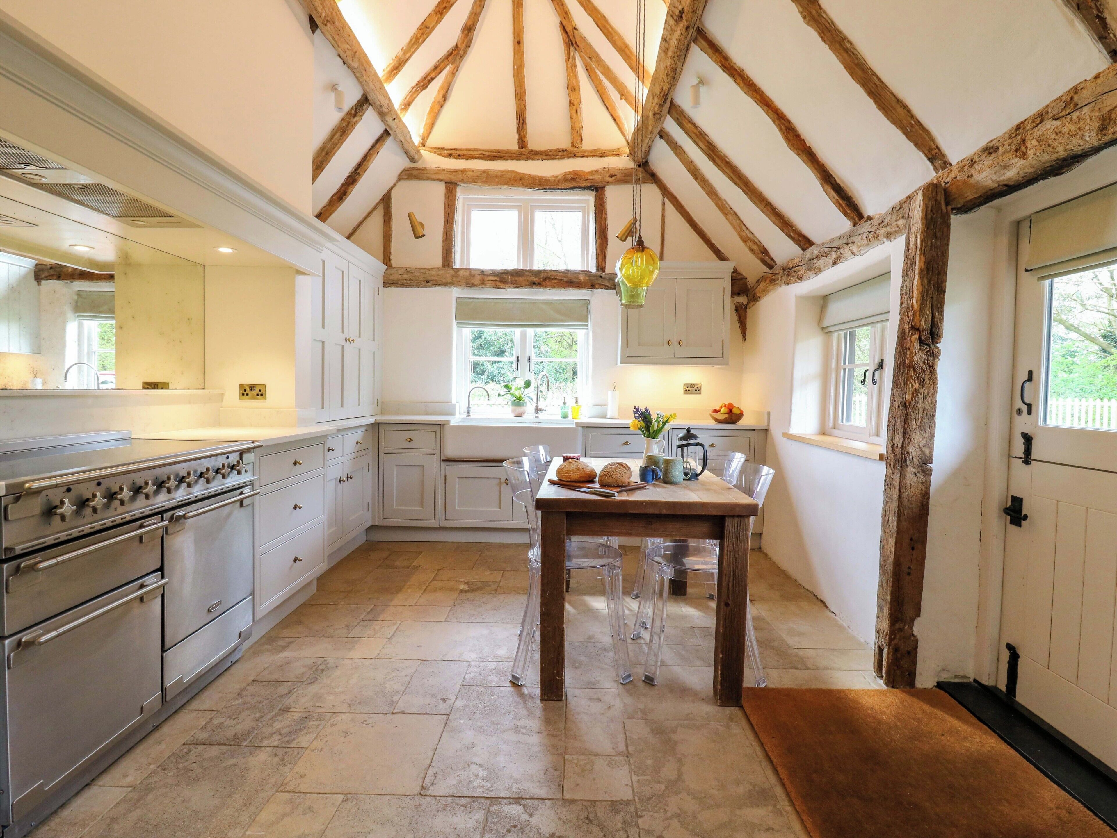 A kitchen with a large stove, wooden beams, white cabinets, and a dining table with clear glasses.