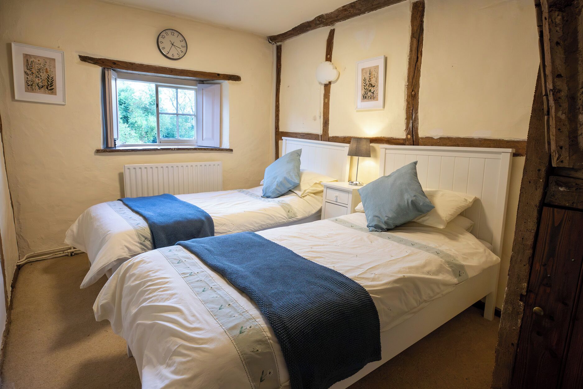 A bedroom with two beds, a window, a clock, and a radiator.