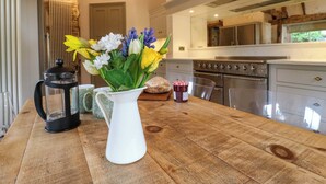 A wooden table with a white pitcher of flowers, a black lantern, and a jar of jam. - Manor Farm Cottages (Milton Keynes)