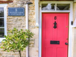 A red door with the number 8, a stone wall, and a sign for Manor Farm Cottages.