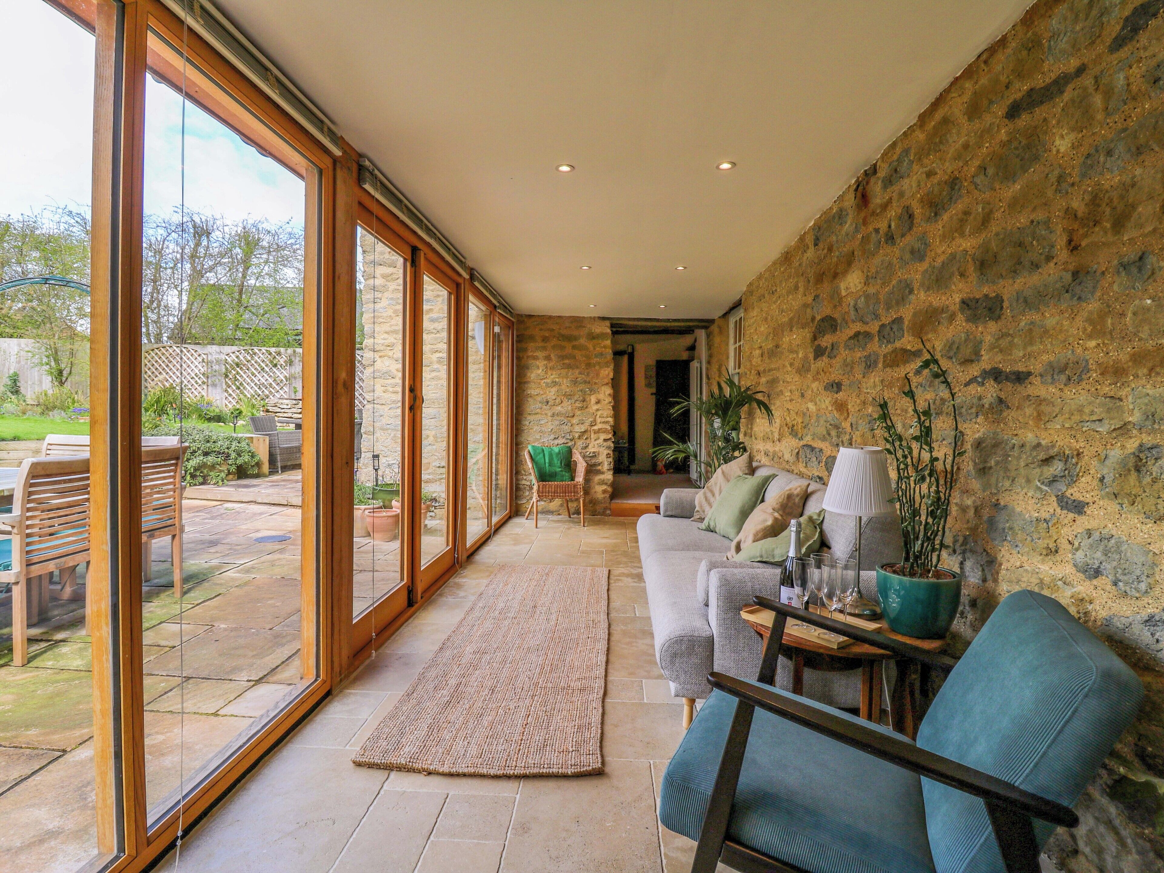 A spacious room with a stone wall, a large sliding glass door leading to an outdoor patio, a sofa, and a small table with a lamp.