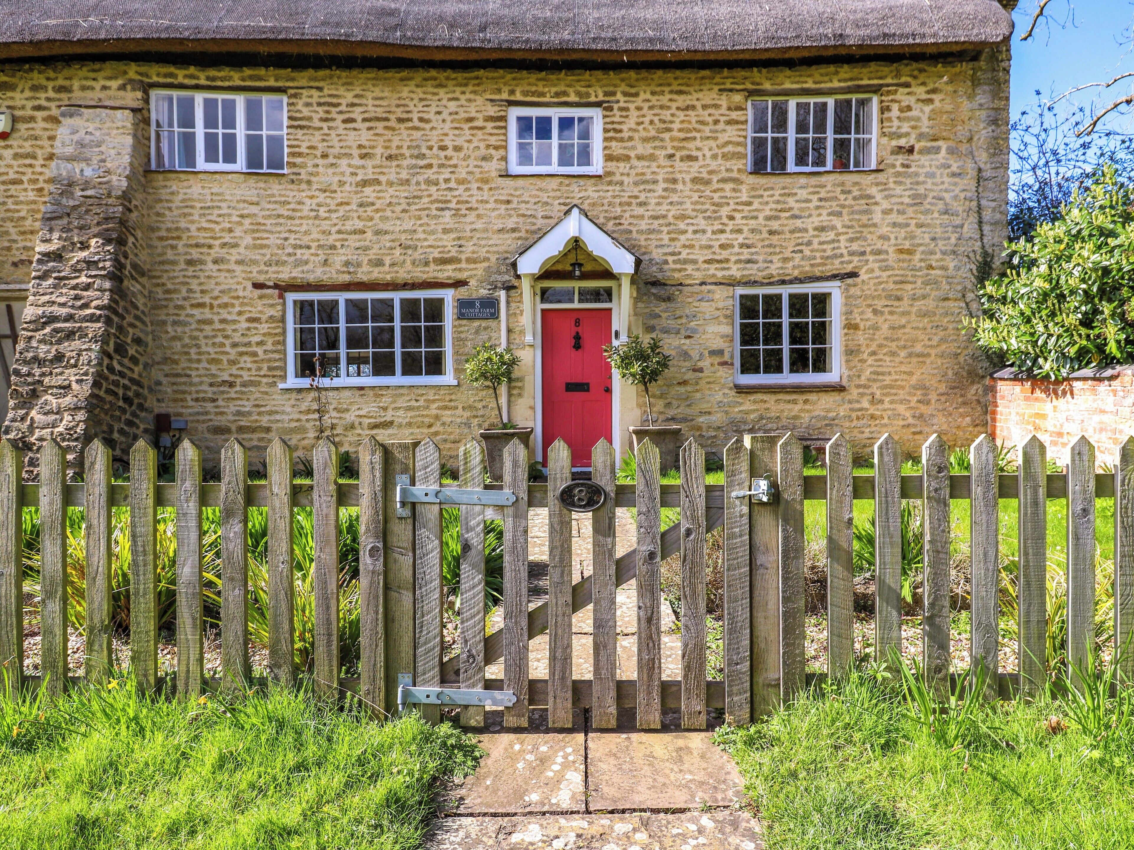 A stone cottage with a red door, a wooden picket fence, and a small garden.