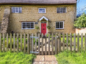 A stone cottage with a red door, a wooden picket fence, and a small garden. - Manor Farm Cottages (Milton Keynes)