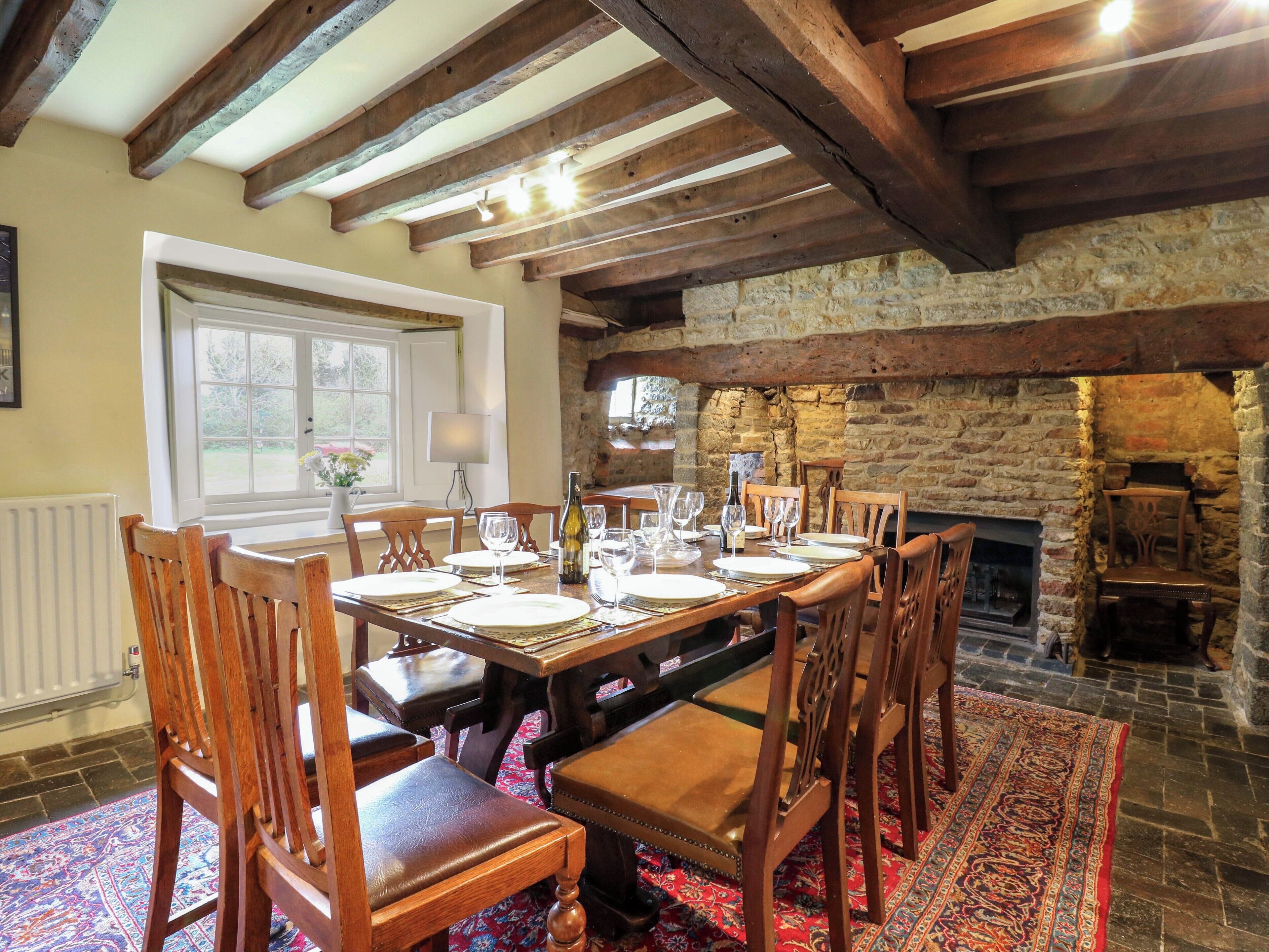 A dining room with a stone fireplace, wooden beams, and a table set for six.