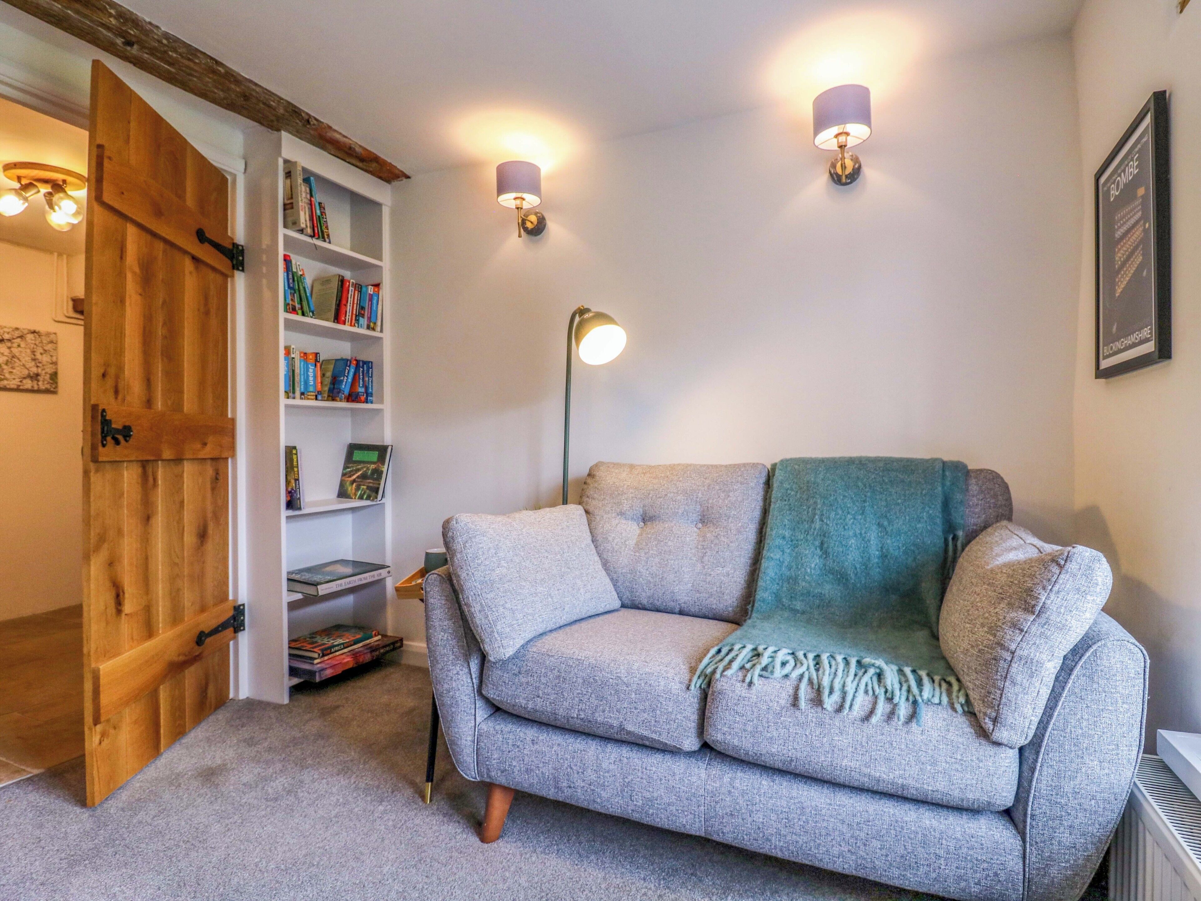 A cozy room with a grey sofa, a wooden door, a bookshelf, and two wall-mounted lamps.