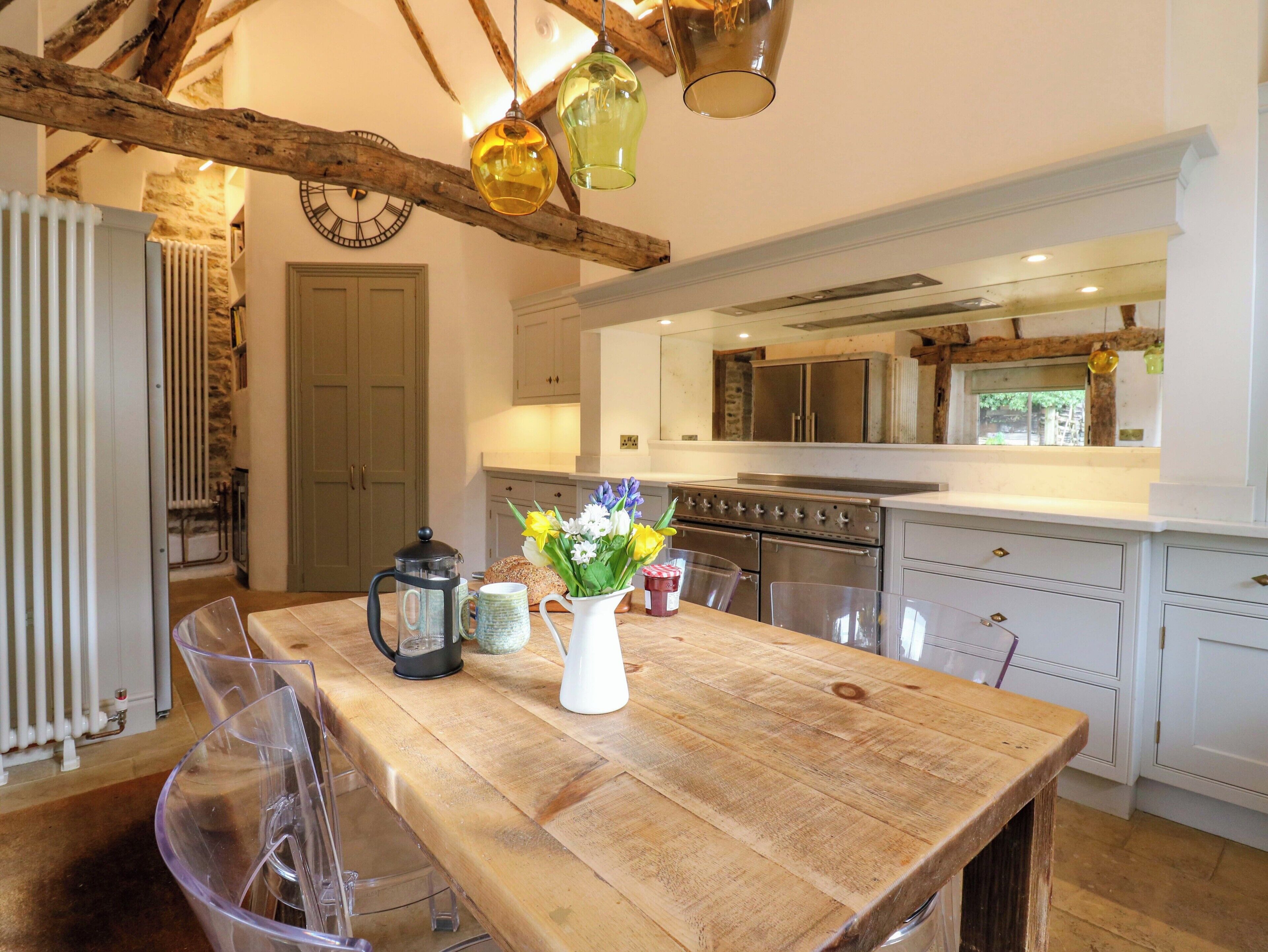 A kitchen with a wooden table, clear chairs, a coffee pot, a pitcher, and a vase with flowers.