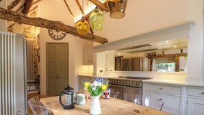 A kitchen with a wooden table, clear chairs, a coffee pot, a pitcher, and a vase with flowers. - Manor Farm Cottages (Milton Keynes)