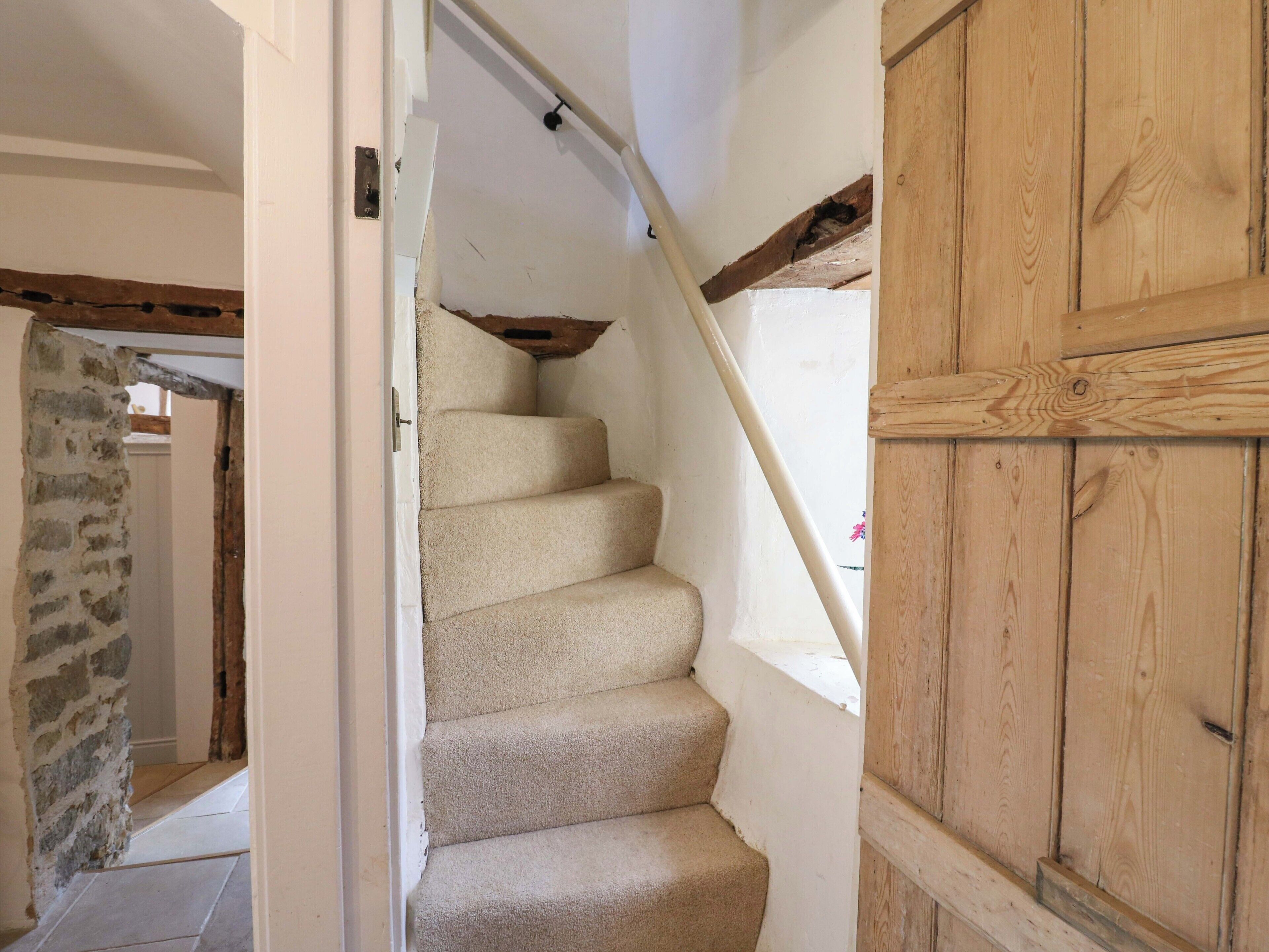 A staircase with beige carpet, white walls, and exposed wooden beams.