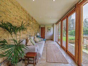 A room with a stone wall, a sofa, a small table, and a large window.