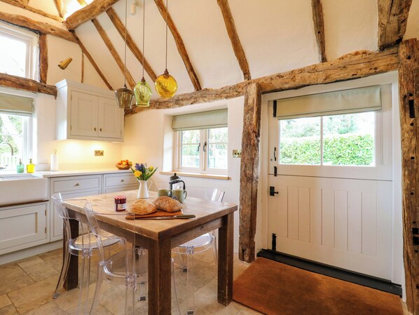 A rustic kitchen with wooden beams, a dining table with chairs, a window with a view, and a door.