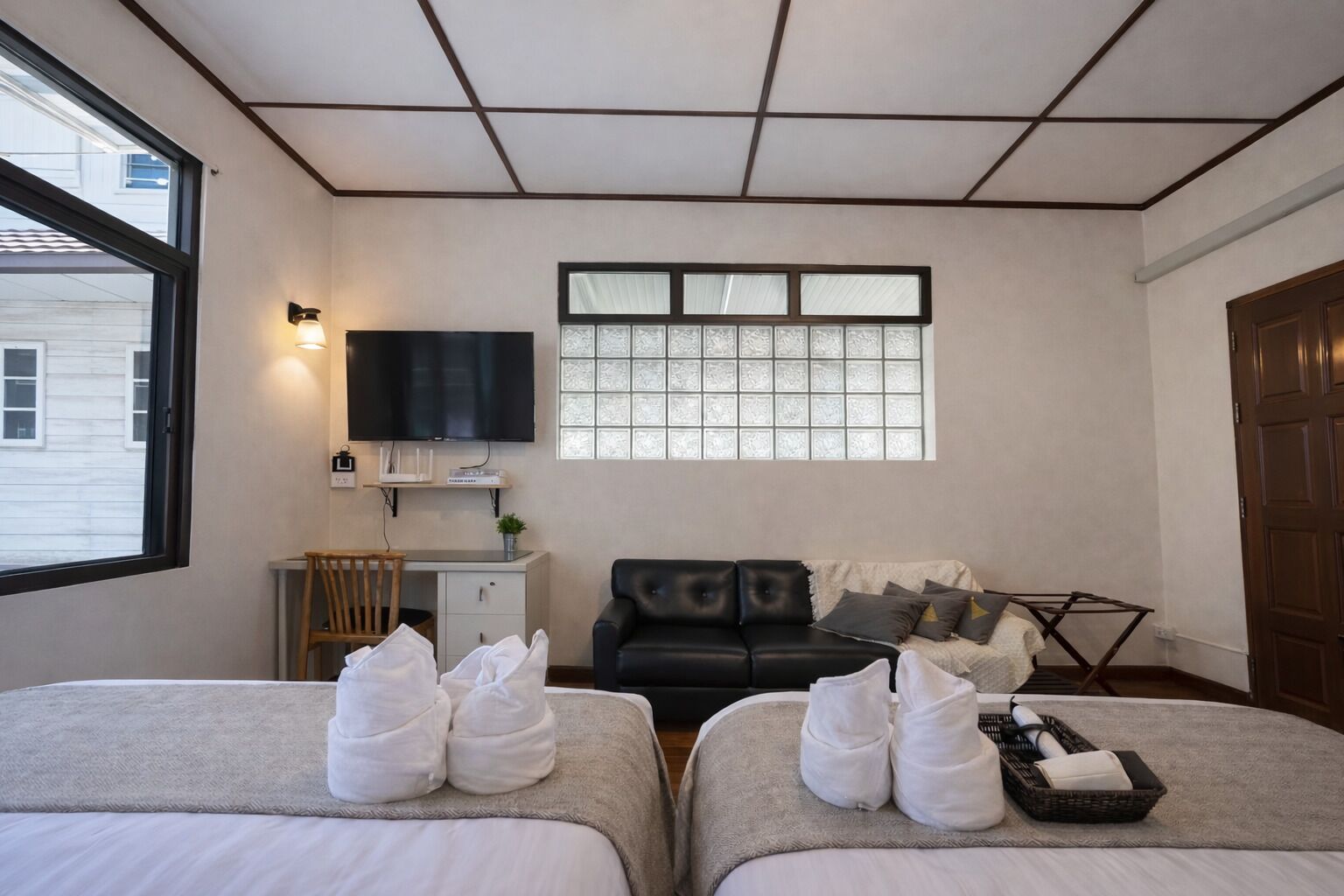 A hotel room with two beds, a desk, a television, a window, and a door.