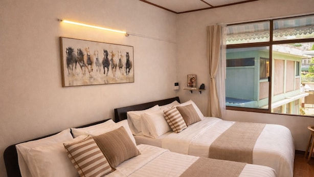 Ein Hotelzimmer mit zwei Betten, einem Bild an der Wand, einem Fenster mit Aussicht und einem kleinen Tisch am Fenster.