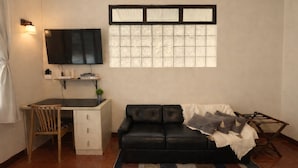 Ein Wohnzimmer mit einer schwarzen Ledersofa, einem Holzstuhl, einem an der Wand montierten Fernseher und einem Fenster mit dekorativen Glasfeldern.