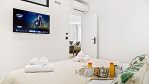 Habitación de hotel con una cama, televisor montado en la pared, bandeja con artículos de desayuno y puerta que da a otra habitación.