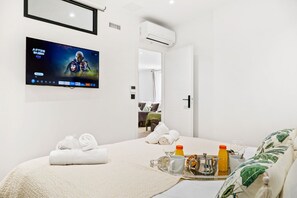 Une chambre d’hôtel avec un lit, un téléviseur fixé au mur, un plateau avec des articles pour le petit-déjeuner et une porte donnant sur une autre pièce.