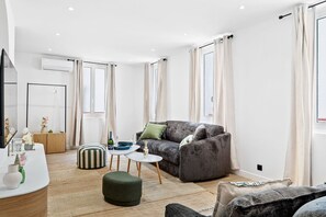 Un salon moderne avec un canapé gris, une table basse ronde et un pouf à rayures.