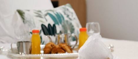 A neatly made bed with a rolled white towel, a tray with croissants and orange juice, and a plastic bag with a logo.