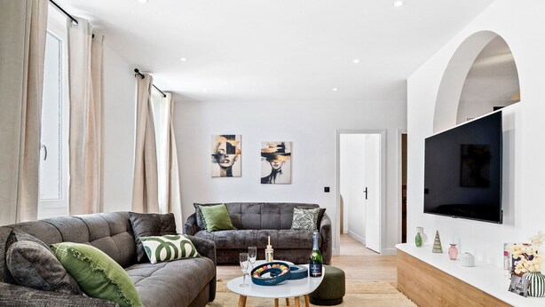 Un salón moderno con un sofá gris, una mesa de centro y un televisor montado en la pared.