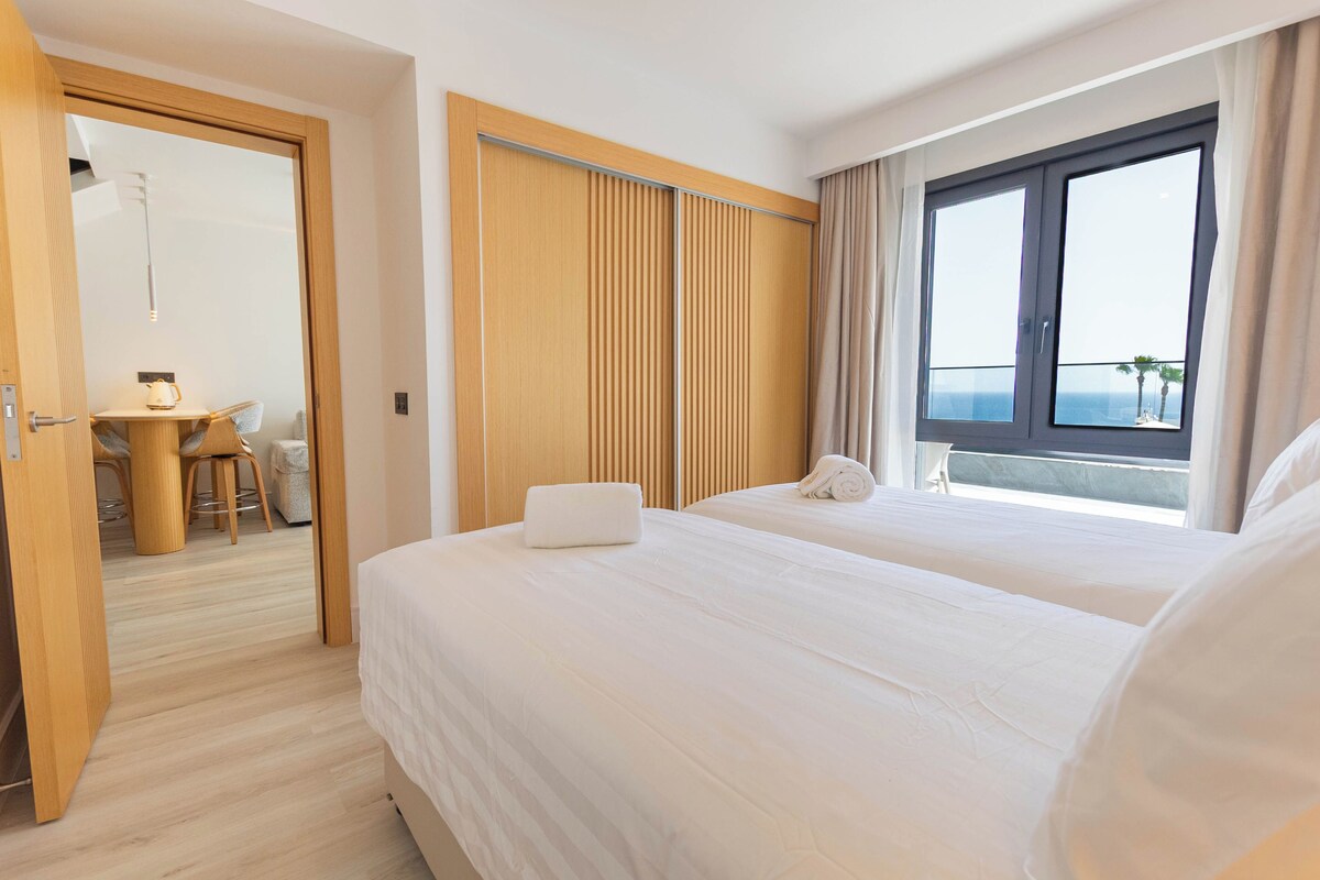 Une chambre d’hôtel avec deux lits, une armoire en bois, une petite table avec des chaises et une fenêtre donnant sur un paysage agréable.