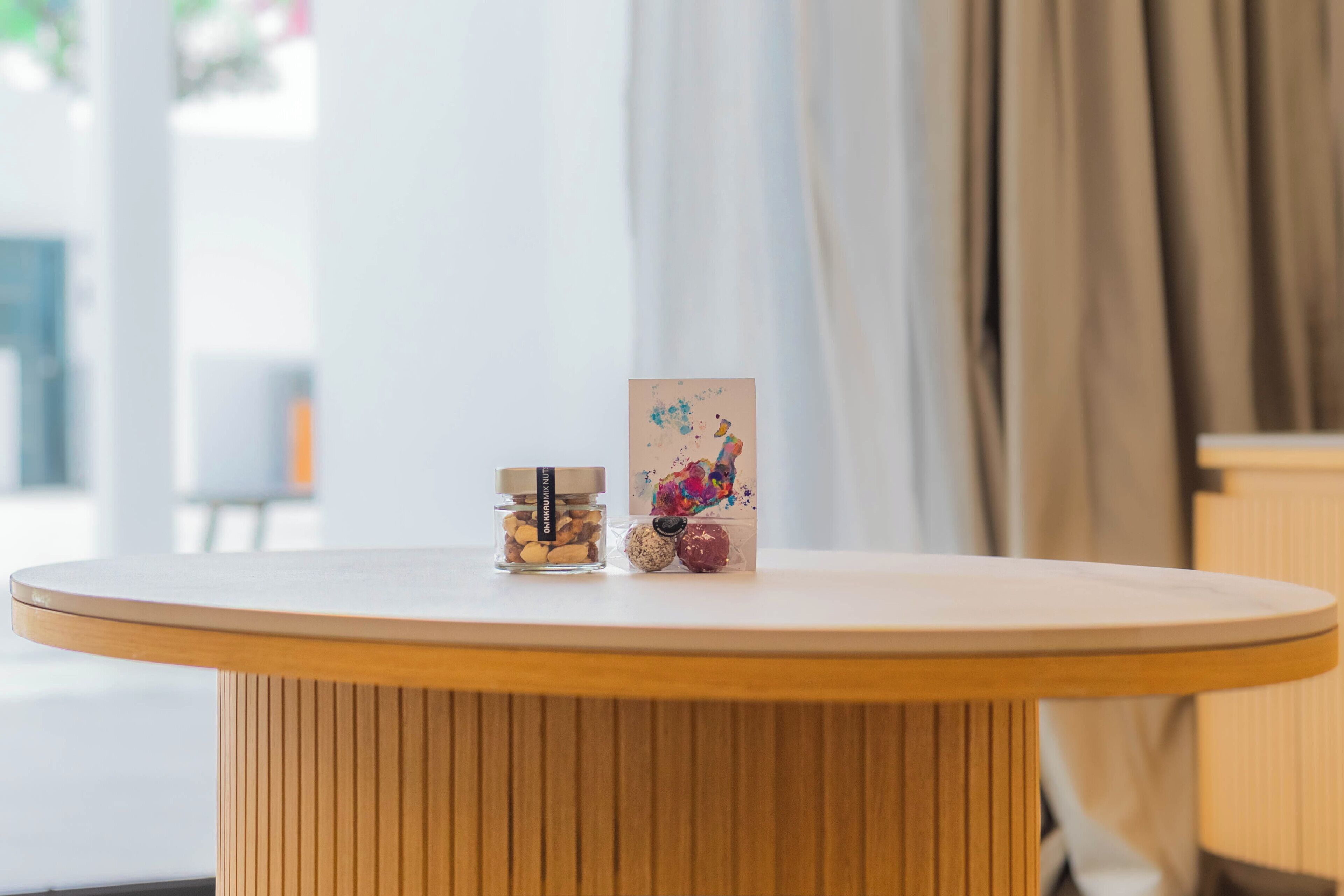 Une table ronde en bois avec un plateau blanc, un petit bocal en verre muni d’une étiquette et un objet décoratif aux motifs colorés.